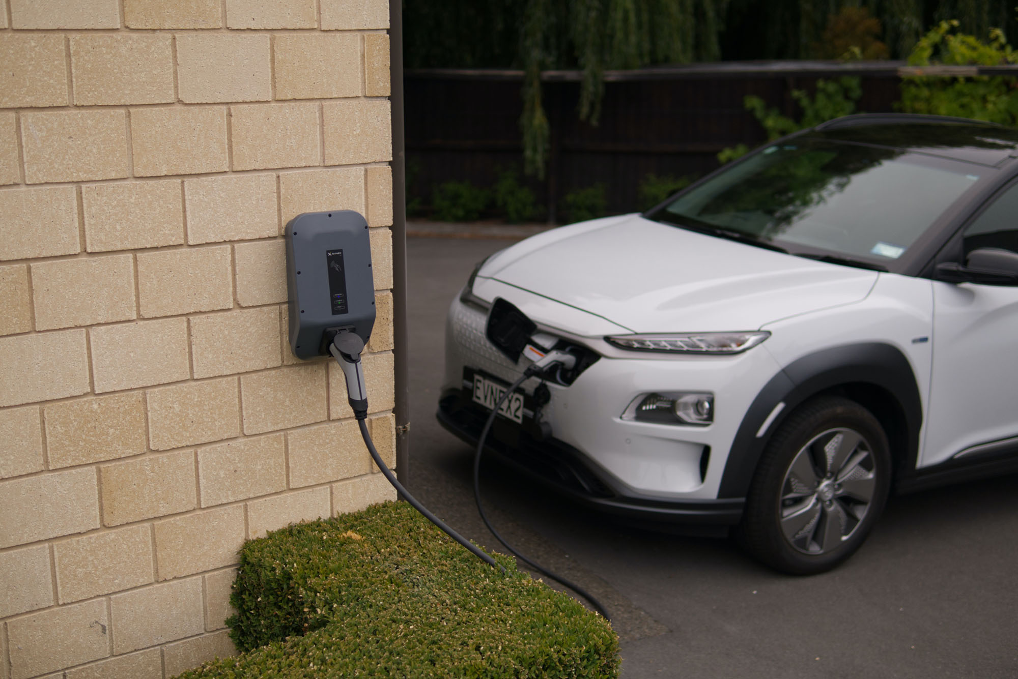 Laadpaal aan muur met elektrische wagen in achtergrond